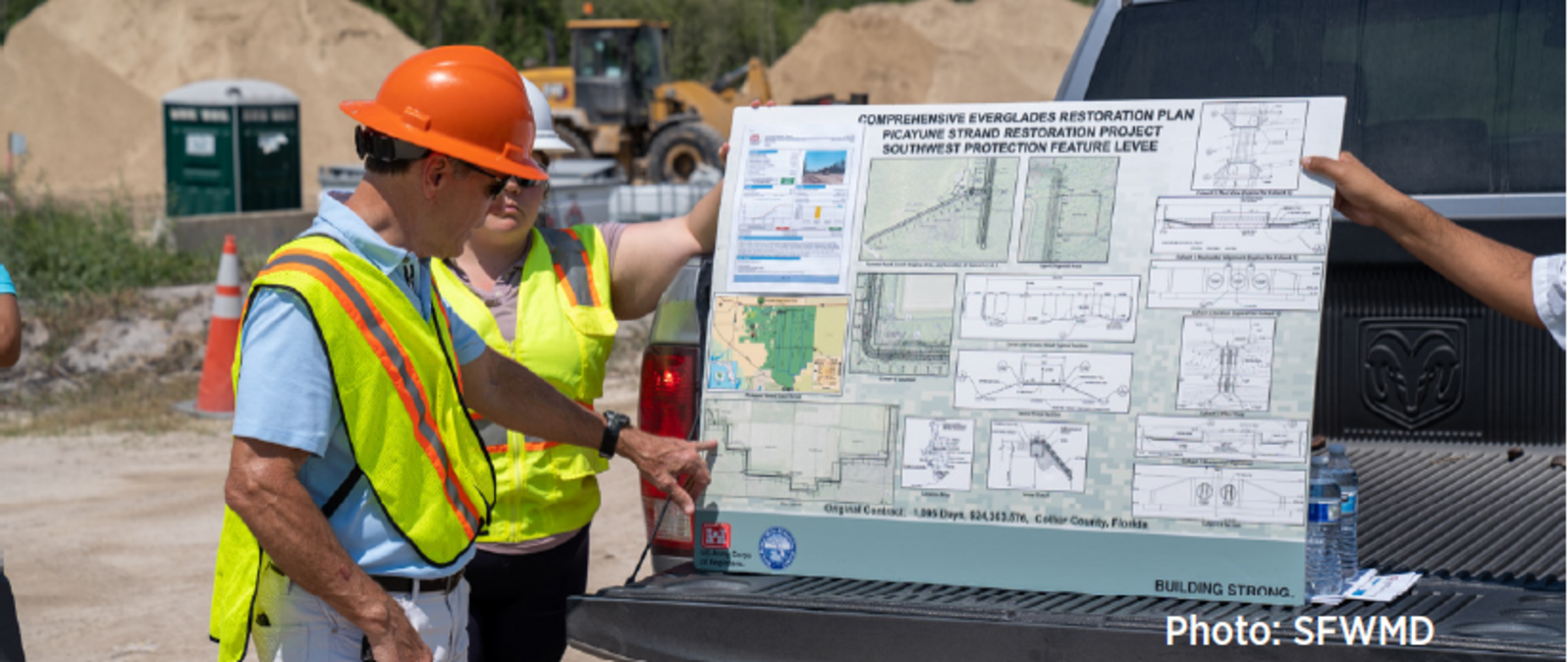 A man in a hardhat and safety vest points to a large map of the CERP in the back of a pickup truck.
