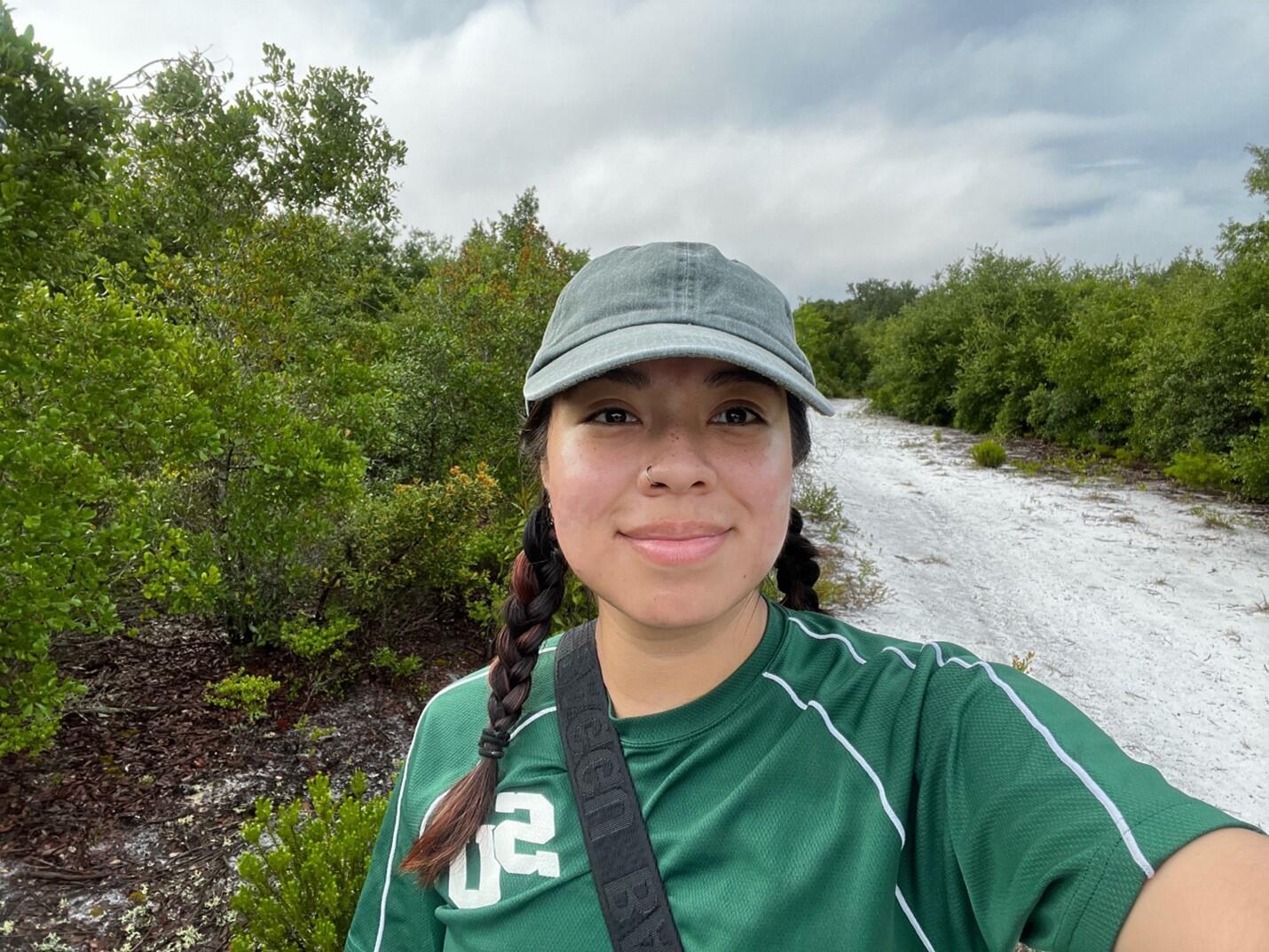 A selfie of a woman wearing a hat on a sandy trail.