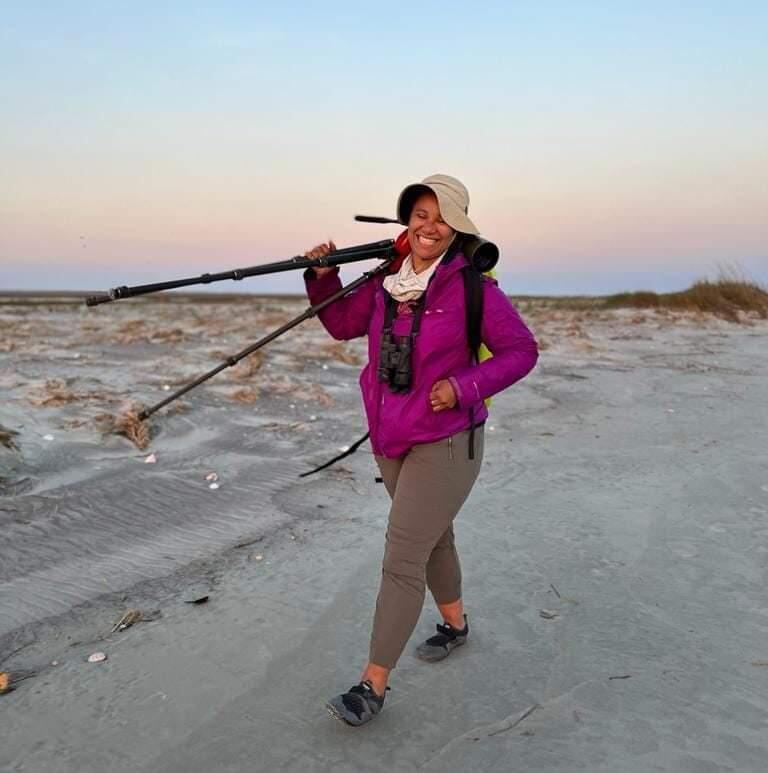 Natasza on a beach, carrying a scope over her shoulder.