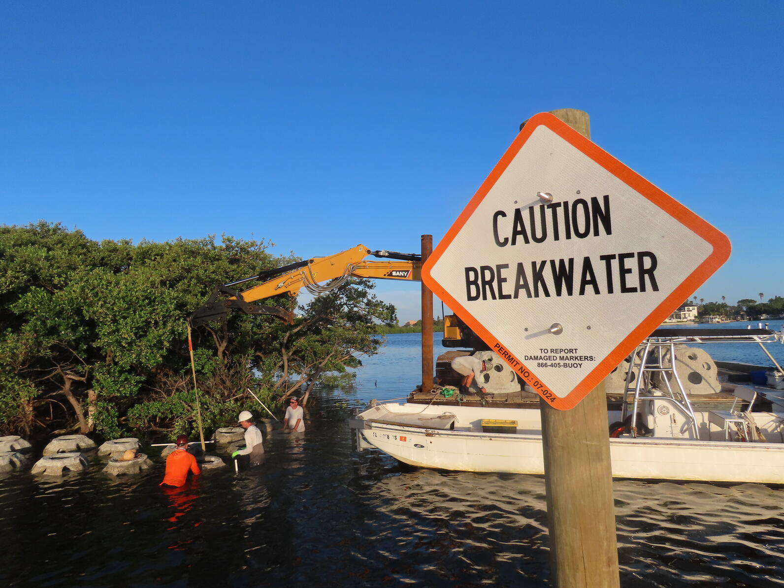 Heavy equipment loading concrete structures next to a sign saying "Caution Breakwater"