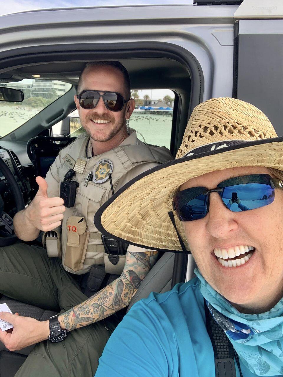 An officer in a truck gives a thumbs-up and smiles in a selfie taken by a volunteer bird steward beside him.