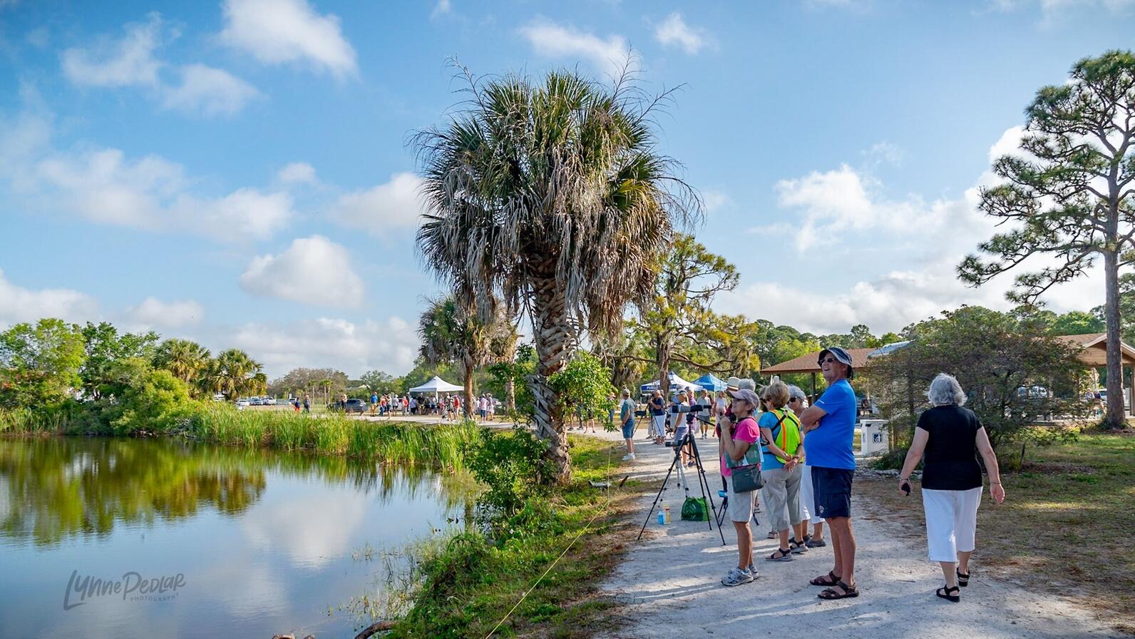 Dozens of birders gather around the shore of a lake during the Rookery Day event.