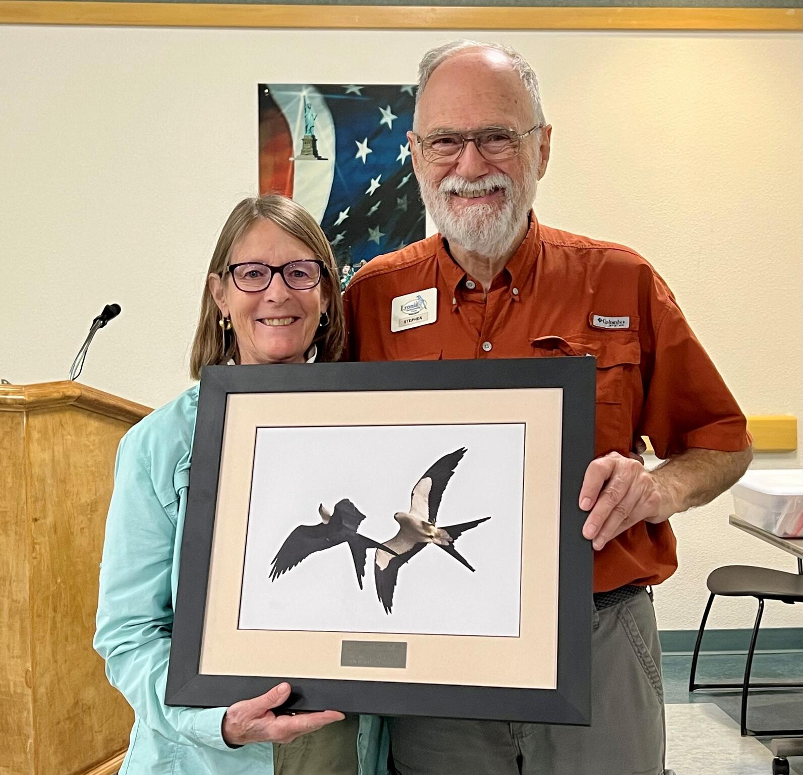 Jacqui Sulek and Stephen Kintner stand together, holding Stephen's award: a framed photo of two Swallow-tailed Kites in flight, with a plaque at the bottom.