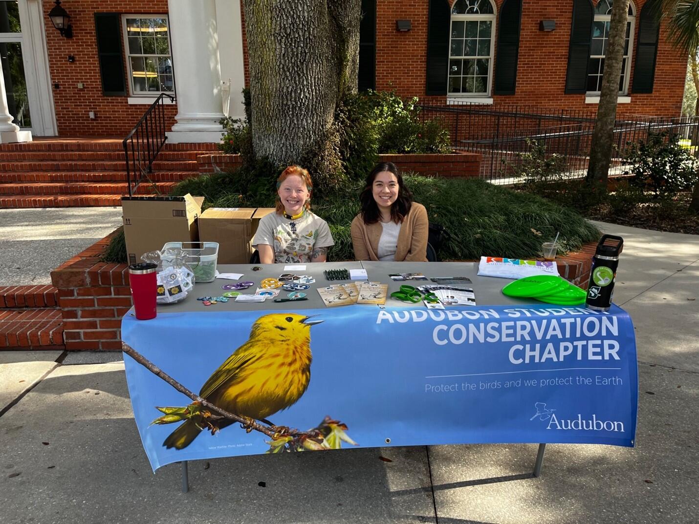 Two women sit at an information table with a sign that reads "Audubon Student Conservation Chapter."