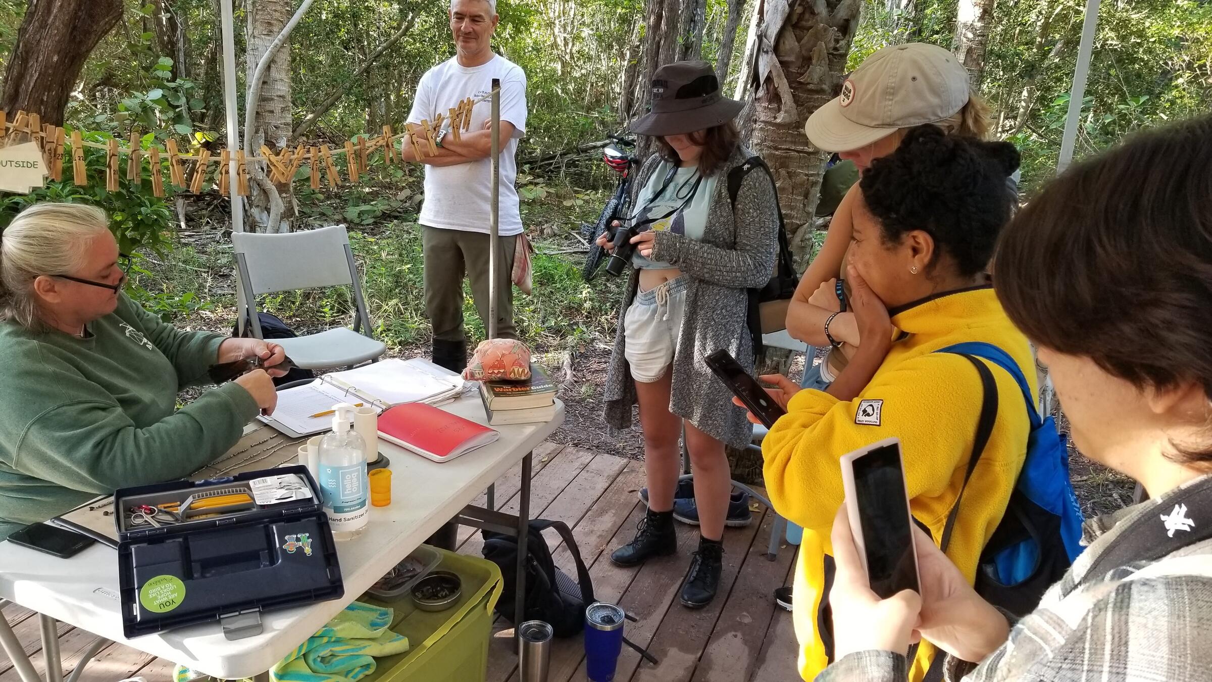 Conservation Leadership Initiative students visit bird-banding sites to learn more about research and conservation. Photo shows students gathered around a table where someone holds a bird.