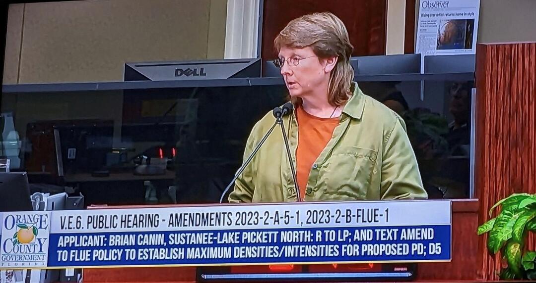 A screenshot of a televised county commission meeting where a woman is speaking.