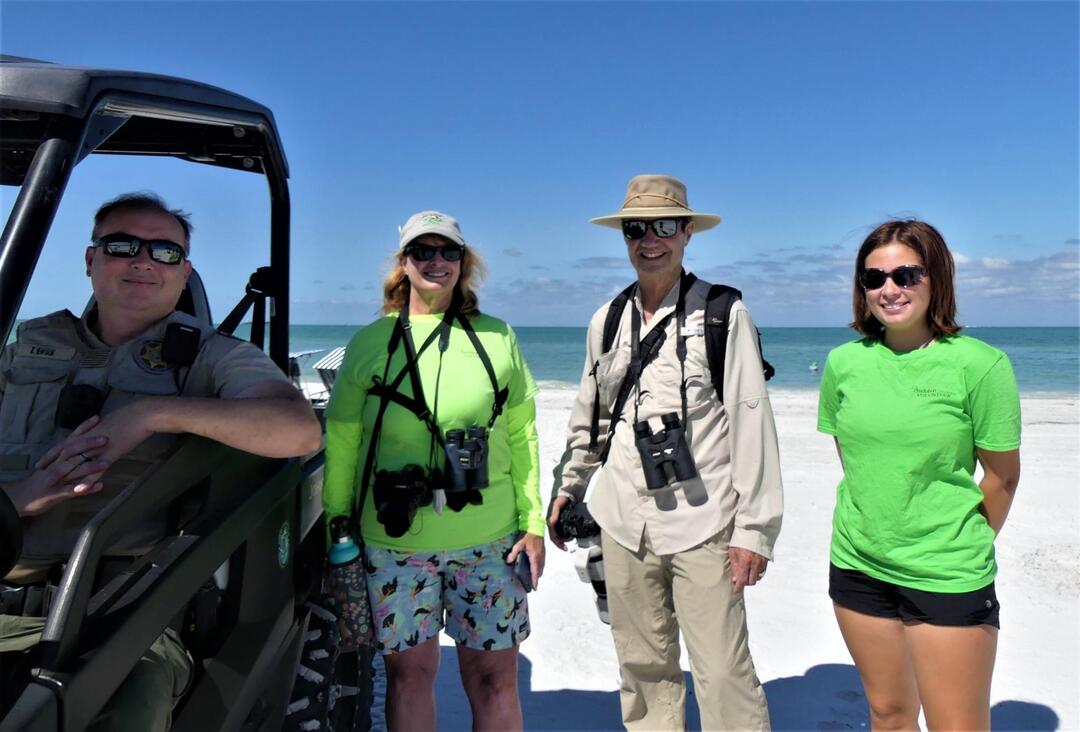 Three bird steward volunteers stand on the beach next to an officer sitting in a beach vehicle.